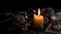Mystical candle flame illuminates crystal collection with tarot cards and herbs for spiritual meditation, divination and healing rituals on dark background.