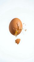Cracked brown chicken egg with yolk and white spilling out on clean white background. Isolated breakfast ingredient for cooking and baking projects.