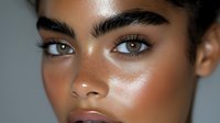 Close-up portrait of young mixed-race woman with natural glowing skin, defined eyebrows and subtle makeup looking directly at camera for beauty concepts.