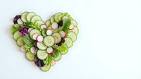 Fresh cucumber and radish slices arranged in heart shape with green herbs on white background for healthy eating and food styling projects.