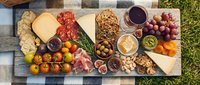 Charcuterie board with cured meats, cheeses, crackers, fresh fruits, nuts, and wine arranged on wooden surface for entertaining and gatherings.