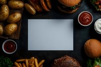 Blank gray card mockup surrounded by burgers, french fries, potatoes and sauces on dark background. Food frame with copy space for menu or restaurant design.