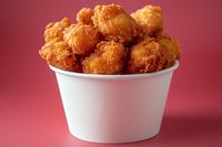 Crispy golden chicken nuggets piled high in white takeout container against vibrant pink background, showcasing appetizing fast food presentation for menu and advertising.