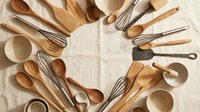 Wooden kitchen utensils arranged in circular pattern on linen cloth. Natural bamboo and wood cooking tools including spoons, whisks, spatulas for culinary use.