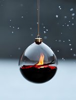 Glass Christmas ball ornament with burning flame inside against snowy winter background, creating dramatic contrast between fire and ice elements.