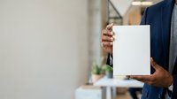 Businessman in dark suit holding blank white paper document or certificate in office environment with blurred background for corporate messaging.