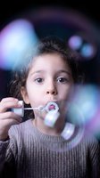 Young girl blowing soap bubbles with colorful bokeh lights creating magical atmosphere for childhood and play concepts.