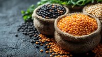 Raw red and black lentils in rustic burlap sacks on dark stone background with scattered legumes and fresh herbs, macro food photography for cooking blogs.