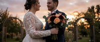 Happy newlywed couple sharing intimate moment during golden hour sunset with bridal bouquet in vineyard setting for wedding photography and romance.