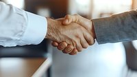 Close-up view of business professionals shaking hands in office setting, symbolizing partnership, agreement, and successful negotiation. Soft background blur creates professional atmosphere.