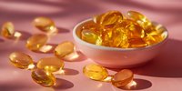 Golden omega-3 fish oil capsules in white bowl on pink background, nutritional supplement for heart health and cognitive function.