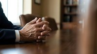 Professional businessman hands clasped on wooden conference table during corporate meeting or negotiation in modern office boardroom setting.