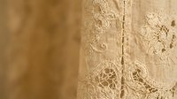 Vintage lace fabric with intricate floral embroidery and delicate patterns in warm beige tones for wedding dress design and romantic textile projects.
