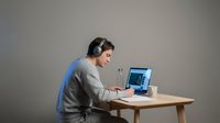 Young man with headphones working on laptop at wooden desk in modern office space for remote work and productivity.