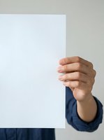 Hand holding blank white card or paper sheet against neutral background for advertising message or promotional content.