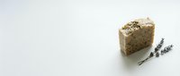 Natural handmade soap bar with herbs and lavender sprigs on clean white background for organic skincare and spa wellness products.