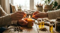 Hands crafting natural orange pomander with cloves and spices on rustic wooden table. Cozy autumn winter holiday preparation scene with warm lighting.