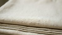Natural linen fabric stack with soft beige texture, organic cotton material for home decor, clothing design and craft projects.