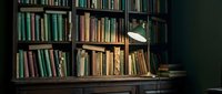 Vintage library interior with wooden bookshelves filled with old books and classic desk lamp creating warm atmospheric lighting for reading and study.