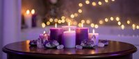 Purple advent wreath with four lit candles on wooden table creating warm holiday atmosphere with bokeh lights background for Christmas decoration.