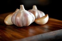 Fresh garlic bulbs and cloves on wooden cutting board for cooking and culinary preparation in kitchen setting.