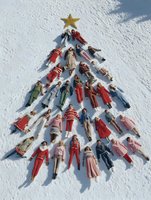 Group of people lying in snow forming Christmas tree shape with golden star on top during winter holiday celebration outdoors.
