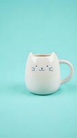 Cute white ceramic cat mug with whiskers and ears on turquoise background for kitchen decor and beverage enjoyment.