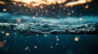 Underwater split view with golden bokeh particles floating above and below surface. Turquoise ocean water with sunlight creating magical atmosphere. Suitable for nature backgrounds.