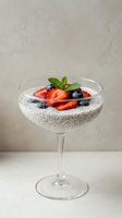 Chia seed pudding dessert in coupe glass topped with fresh strawberries, blueberries and mint leaves. Healthy breakfast or vegan dessert option for food and wellness content.