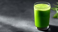 Fresh green smoothie in glass on dark stone surface with spinach leaves for healthy lifestyle and detox nutrition.