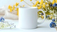 White ceramic mug mockup surrounded by yellow and blue wildflowers on light background, perfect for product presentation and branding projects.