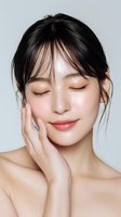 Young Asian woman with closed eyes touching face, showcasing glowing skin and natural makeup against white background. Perfect for skincare advertising.