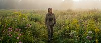 Young Caucasian male hiker walking through wildflower meadow at golden hour sunrise. Outdoor adventure and nature exploration concept for wellness campaigns.