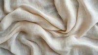 Soft beige linen fabric with gentle folds and natural texture creates flowing waves and wrinkles, showing organic movement in natural light.
