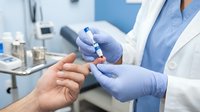 Healthcare professional in white coat and blue gloves performing blood glucose test on patient's finger in modern medical clinic setting.