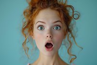 Young woman with red curly hair and bright blue eyes expressing surprise with open mouth against turquoise background, showing genuine emotion and amazement.