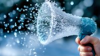 Megaphone spraying water droplets in frozen motion against blue background, creating dynamic splash effect with bokeh lights for advertising and announcement concepts.