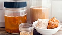 Homemade fermented kombucha tea in glass jar with SCOBY mother culture and fresh baked sourdough bread on wooden table, natural probiotics food.