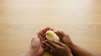 Hands holding fresh baked bread roll on wooden surface. Suitable for bakery, food, nutrition, and hospitality marketing materials.