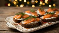 Elegant smoked salmon appetizers on dark bread with cream cheese and dill garnish served on decorative plate with festive bokeh lights background for holidays.