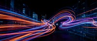 Abstract neon light trails in orange and blue converge and intertwine against dark urban skyline, creating dynamic motion effect for technology and digital design projects.
