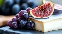 Fresh ripe purple grapes and sliced fig on top of soft brie cheese against dark background, macro food photography for gourmet menu and recipe design.