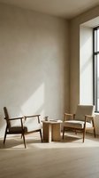 Minimalist living room corner with two wooden armchairs and round table bathed in natural sunlight creating warm shadows on neutral beige walls.