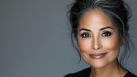 Confident mature Asian woman with radiant smile and elegant makeup against gray background, wearing black top. Natural beauty portrait showcasing graceful aging.