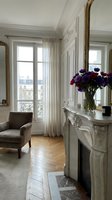 Elegant classic living room with marble fireplace, gold mirror, purple flowers, herringbone parquet floor, and sheer curtains by tall windows.