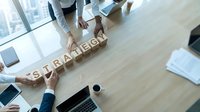 Business team collaborating to spell STRATEGY with wooden letter blocks on conference table during corporate planning meeting.