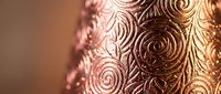 Elegant copper metallic surface with intricate swirl patterns and warm golden lighting creating luxurious decorative texture for premium design projects.