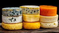 Assorted gourmet cheese wheels stacked on rustic wooden surface against dark background for culinary and food photography projects.