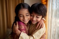 Young Asian siblings sharing tender embrace and genuine smiles, wearing traditional ethnic clothing in warm indoor lighting, expressing pure joy and family bond.