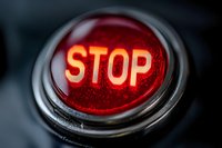 Glowing red stop button with illuminated text on dark background, close-up macro shot showing metallic rim and textured surface. Useful for safety concepts.